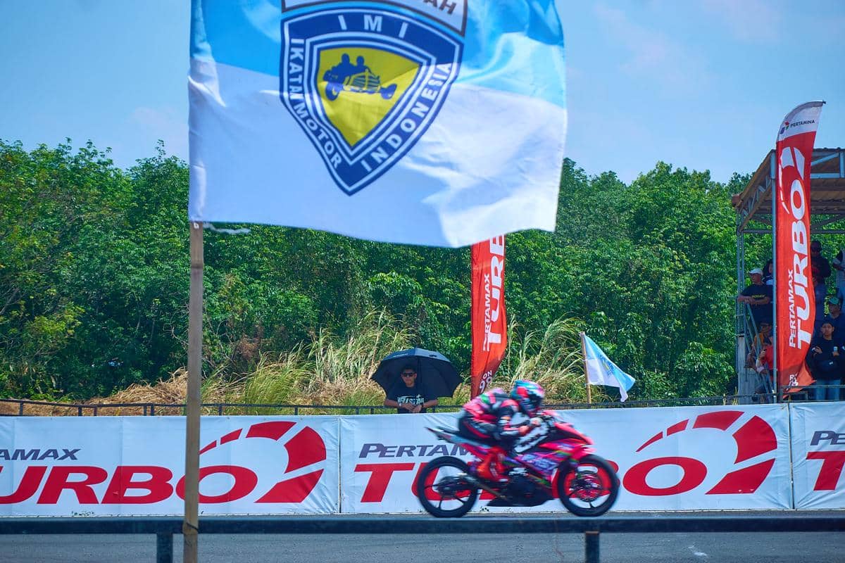 Seorang pembalap melintas di depan pembatas lintasan bertuliskan Pertamax Turbo di bawah kibaran bendera Ikatan Motor Indonesia (IMI) pada F