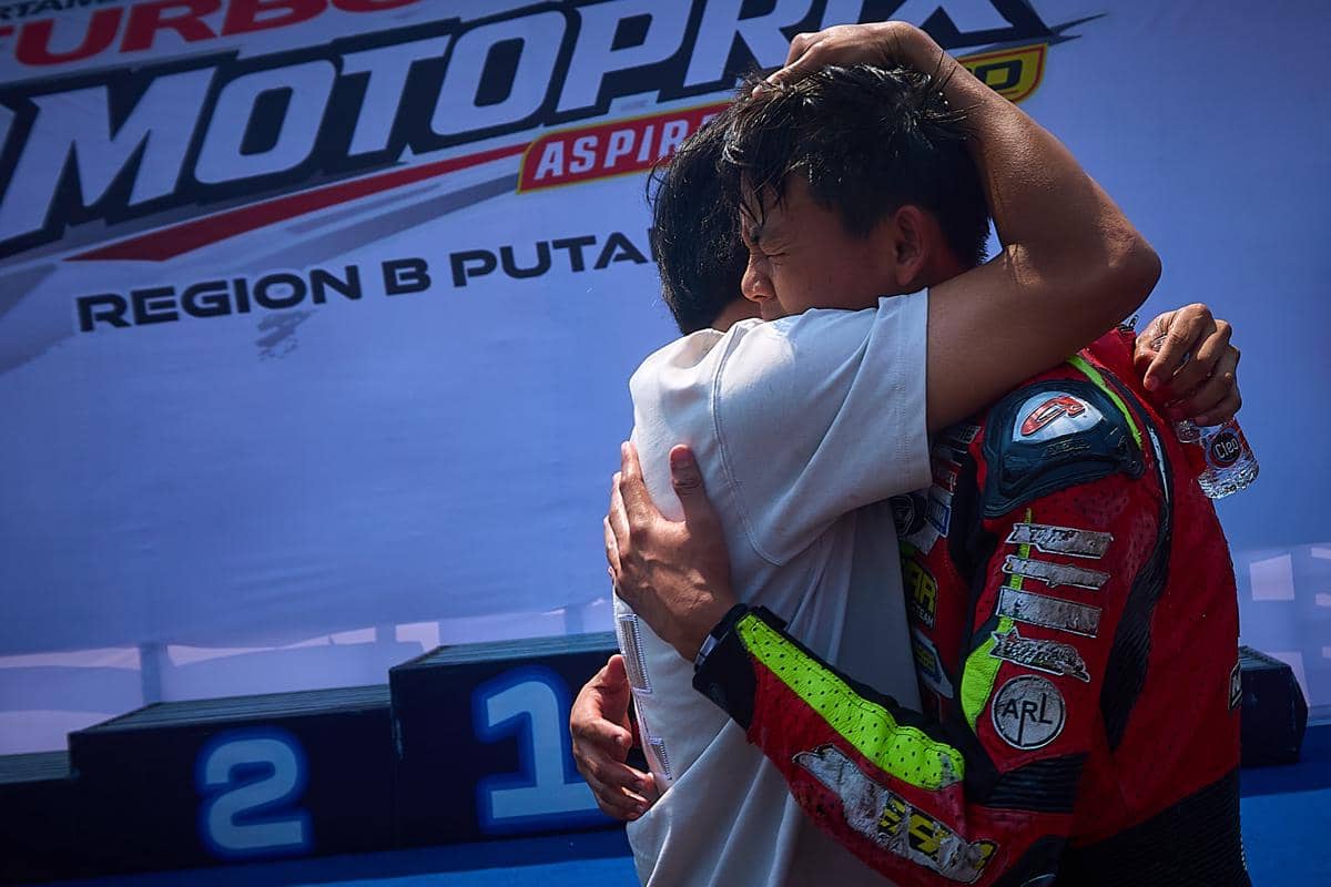 Pembalap remaja Renaldy Junior (15) (kanan), yang masih mengenakan pakaian balap (wearpack), memeluk erat pendampingnya di dekat podium Fina