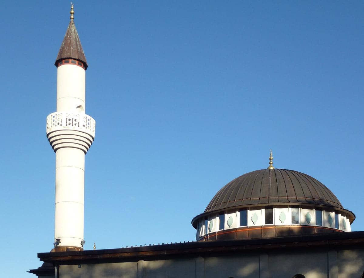 Kubah besar berwarna perak dan menara Masjid Fittja terlihat dari bagian luar bangunan di bawah langit cerah.