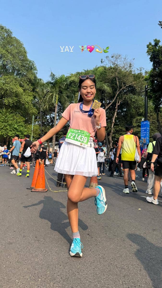 Seorang perempuan berbusana olahraga berpose di area Jakarta Running Festival 2026 dengan suasana acara lari.