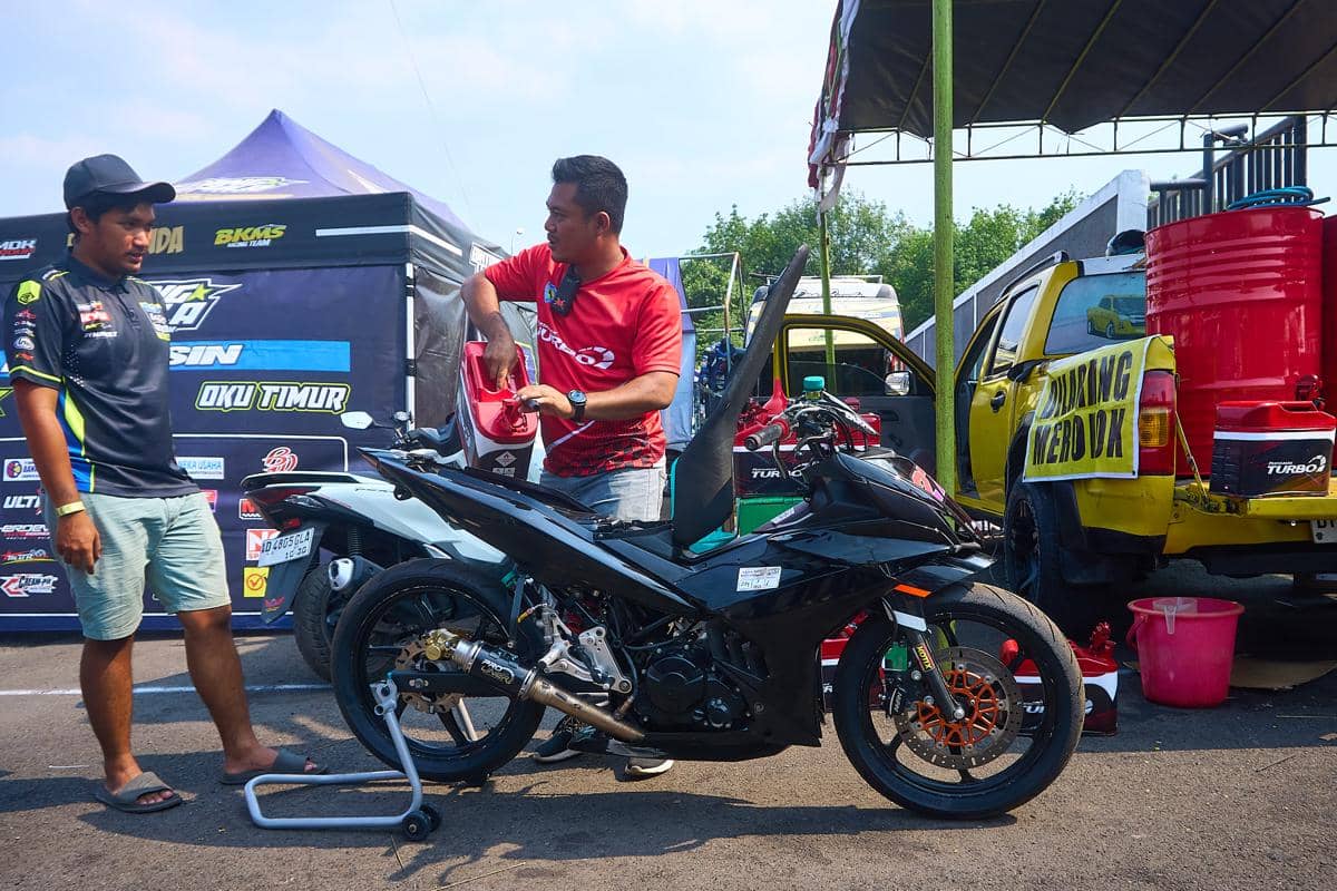 Kru mekanik menuangkan bahan bakar ke dalam tangki sepeda motor balap di atas penyangga (paddock stand) di area paddock Sirkuit Mijen, Kota 
