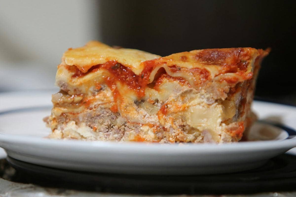 Ilustrasi lasagna berlapis saus dan keju yang dimasak menggunakan slow cooker sebagai hidangan rumahan praktis.