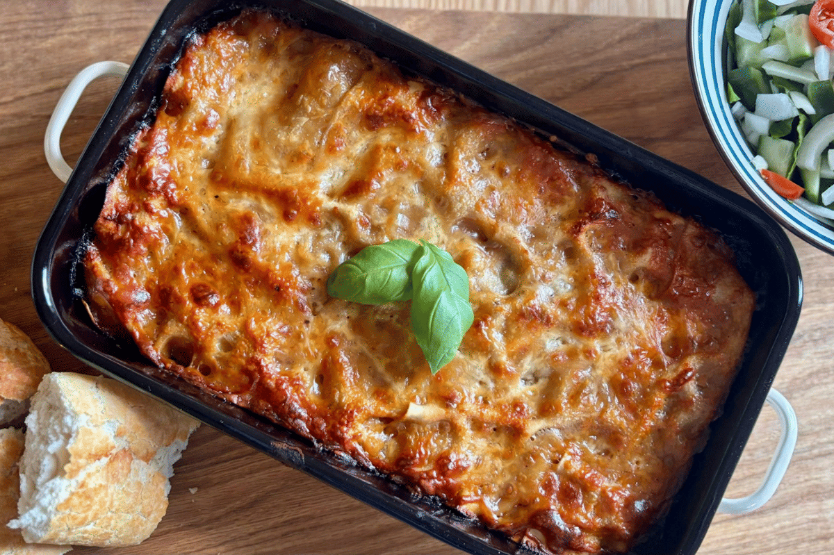 Seporsi lasagna berlapis saus dan keju di dalam slow cooker, disajikan hangat dengan taburan daun hijau.