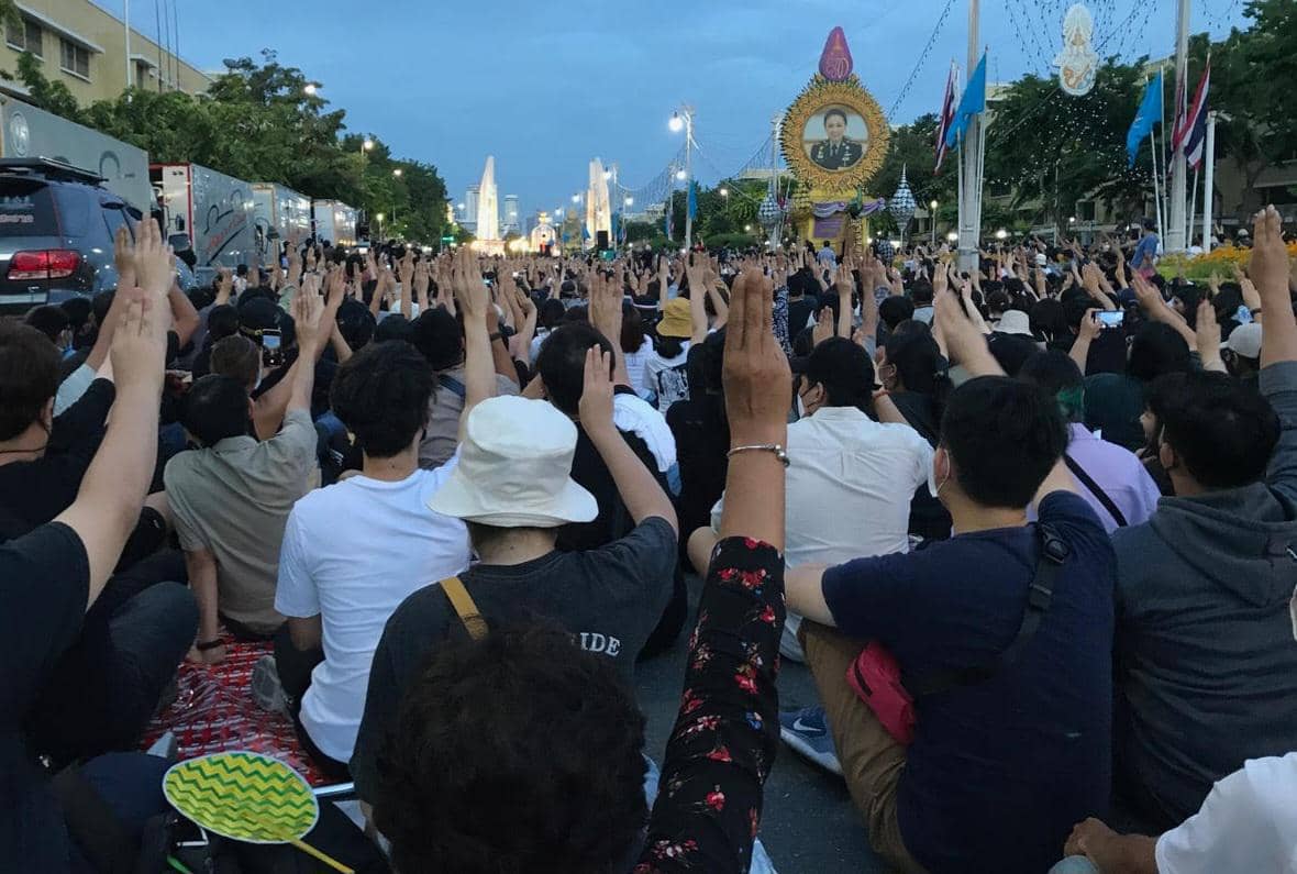 Para pengunjuk rasa mengacungkan salam tiga jari di depan Monumen Demokrasi pada protes 16 Agustus 2020 di Thailand.