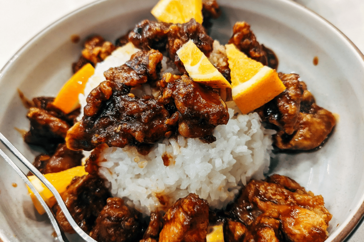 Ilustrasi orange soy sauce pork dengan potongan daging babi bersaus kecokelatan dan irisan jeruk sebagai pelengkap.
