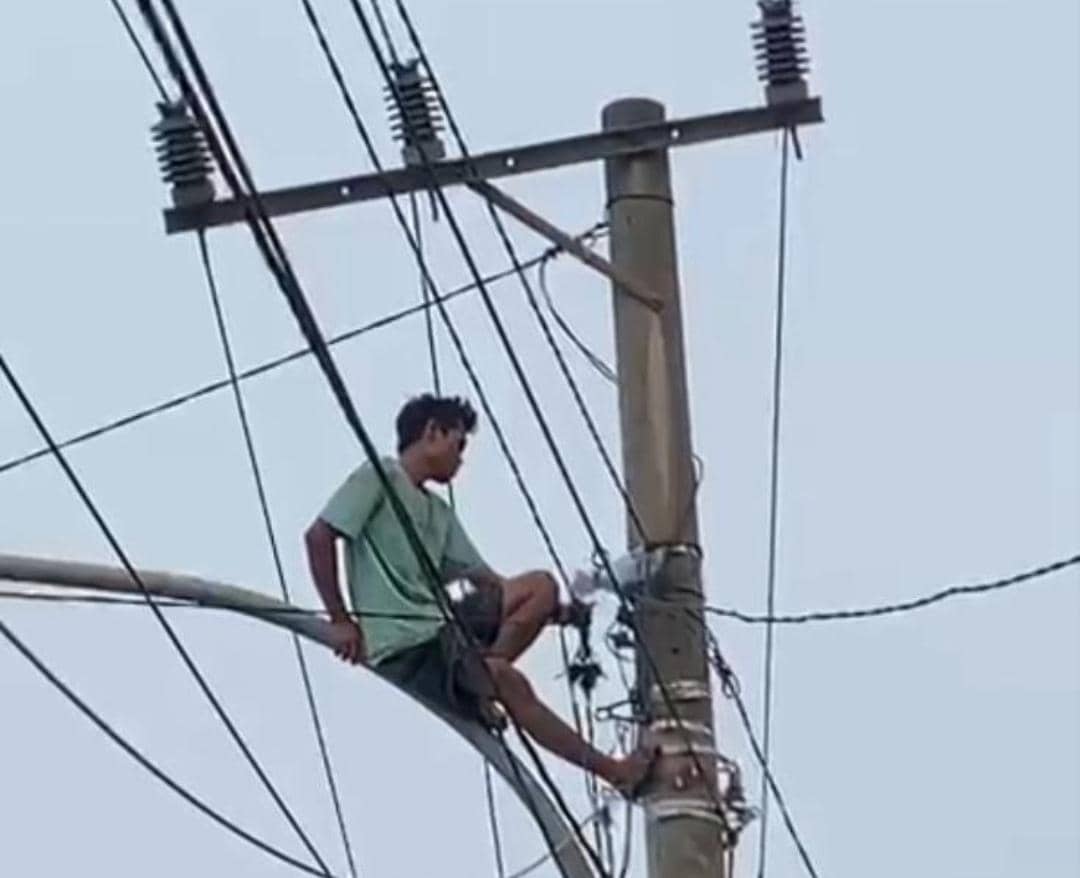 Seorang pria memanjat tiang listrik di Bayung Lencir, tampak berada di antara kabel dan struktur jaringan listrik.